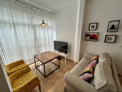 Moderno salón en apartamento CozyHomeSevilla Sevilla con sofá beige, mesa de madera, sillones amarillos, TV y cuadro