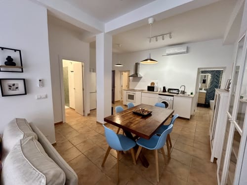 Cocina abierta y comedor en el apartamento Judería3, Sevilla, con mesa de madera, sillas azules y electrodomésticos modernos