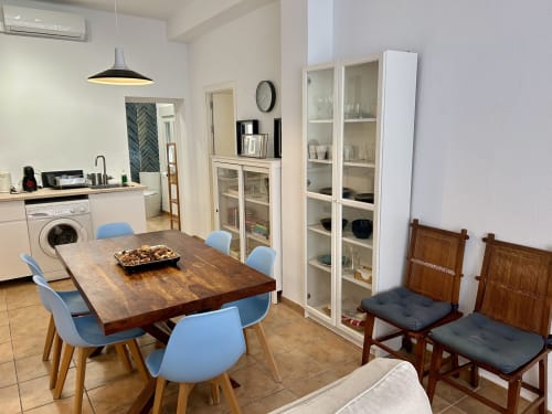 Comedor moderno con mesa de madera y sillas azules, cocina abierta, armarios de vidrio, apartamento Judería3 en Sevilla