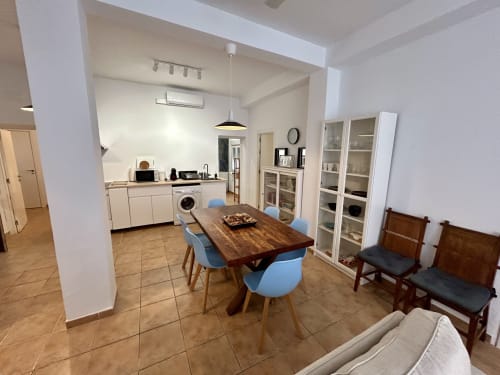 Zona de comedor y cocina integrada en el apartamento Judería3, Sevilla, con mesa de madera, sillas azules y mobiliario blanco