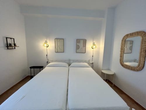 Moderno dormitorio con cama de matrimonio, lámparas colgantes, cuadros enmarcados y espejo de ratán en apartamento Judería3 de CozyHomeSevilla