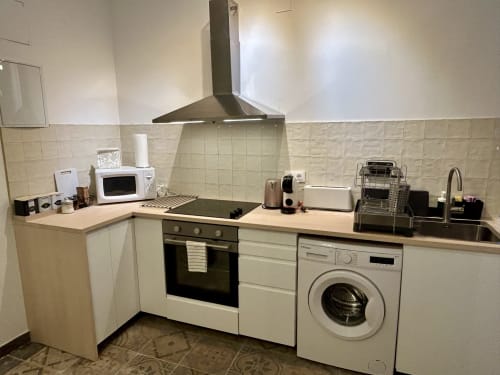 Cocina moderna en apartamento CozyHomeSevilla con muebles blancos, estufa, campana extractora, lavadora y fregadero en Sevilla