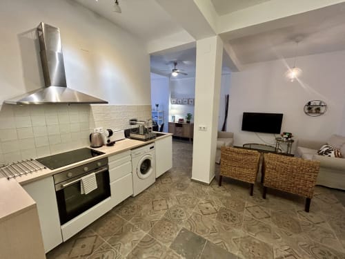 Moderna cocina-salón en apartamento CozyHomeSevilla Sevilla con electrodomésticos acero inoxidable, muebles blancos y texturas tejidas