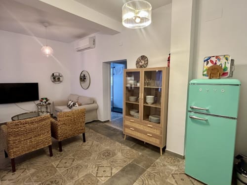 Sala de estar del apartamento CozyHomeSevilla en la Judería con nevera vintage menta, mueble de madera, sillas de mimbre y televisor