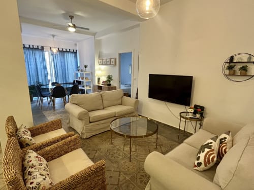Moderna sala de estar en apartamento de Sevilla con sofá crema, sillas de mimbre, televisor y comedor adyacente