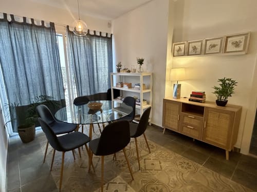 Comedor moderno en apartamento Judería1, Sevilla con mesa redonda de cristal, sillas negras, aparador de madera y cortinas azules
