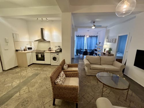 Apartamento moderno en Sevilla con cocina abierta, sala de estar, sillas de mimbre, sofá beige y comedor