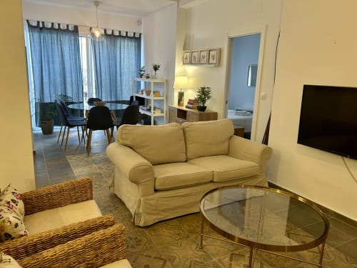 Luminoso salón en apartamento Judería1 de Sevilla, con sofá crema, mesa de cristal y comedor con cortinas azules