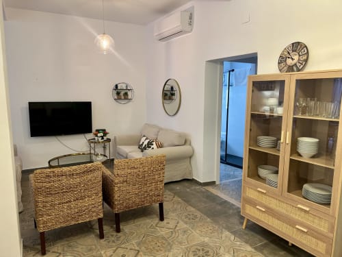 Sala de estar moderna en apartamento CozyHomeSevilla con sillas tejidas, TV, sofá beige y mueble de madera en Sevilla