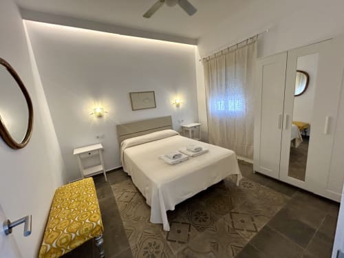 Dormitorio moderno en apartamento CozyHomeSevilla con cama de matrimonio, armario blanco, lámparas colgantes y suelo estampado