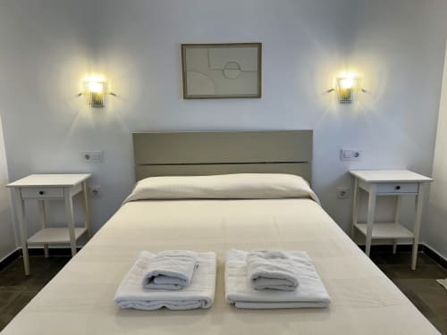 Dormitorio luminoso en apartamento CozyHomeSevilla con cama queen, cabecero verde oliva, mesitas blancas y apliques