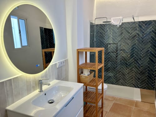 Baño moderno en apartamento CozyHomeSevilla Sevilla con espejo circular iluminado, tocador blanco, ducha con baldosas en espiga