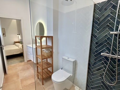 Baño moderno en apartamento de Sevilla con ducha de azulejos en espiga negros, tocador blanco, inodoro, estantes de madera y acceso a