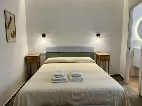 Habitación moderna en CozyHomeSevilla en Sevilla con cabecero verde, mesillas de madera y toallas frescas en la cama