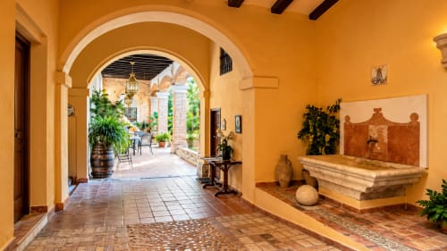 Casa Rural Garden Suites courtyard in Xàtiva with arched colonnade, terracotta tiles, and stone fountain