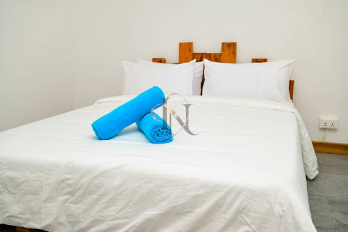 Chambre Nora villa chez Gerards & Angel avec serviettes bleues roulées sur lit blanc, tête de lit en bois, Grand Baie