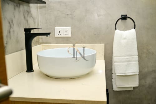 Salle de bain moderne de la villa Gerards & Angel avec lavabo rond blanc, robinetterie noire et porte-serviettes garni de serviettes blanches