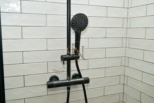 Pomme de douche noire avec douchette à main fixée sur un mur carrelé blanc de style métro dans la salle de bains de la villa Nora chez Gerards &
