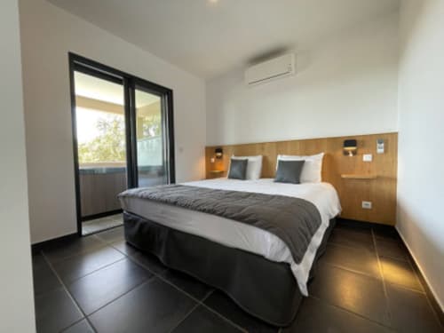 Chambre moderne avec lit queen, tête de lit en bois, carrelage foncé, balcon vue mer et climatisation aux Villas d'A Storia