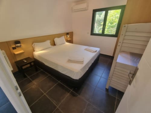 Chambre moderne et lumineuse aux Villas d'A Storia avec lit queen-size, carrelage noir et fenêtre aux volets verts donnant sur Zonza