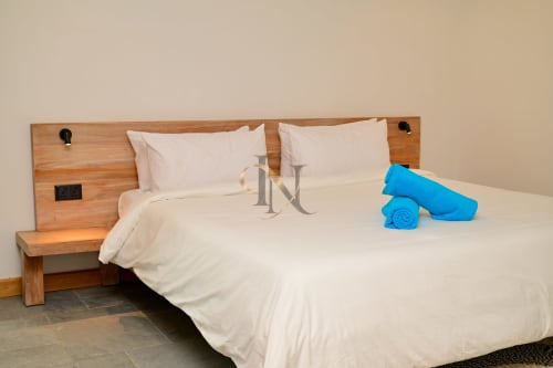 Chambre élégante de villa moderne avec tête de lit en bois, literie crème, oreillers et serviettes bleues à Gerards & Angel, Grand Baie