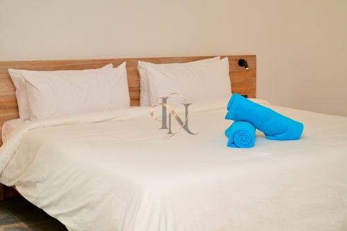 Chambre de la villa Nora à Gerards & Angel, Grand Baie avec draps blancs, tête de lit en bois, serviettes bleues roulées et hôtel