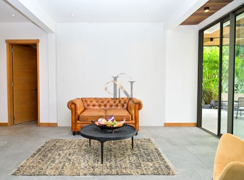 Élégant salon de la villa moderne Gerards & Angel avec canapé Chesterfield beige, table basse noire et vue sur le jardin
