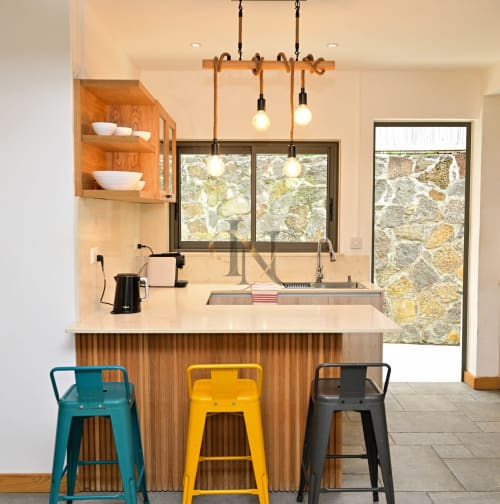Cuisine moderne de la villa Gerards & Angel à Grand Baie avec tabourets colorés, suspensions en bois et vue sur la terrasse en pierre.