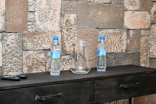 Bouteilles d'eau et pichet en verre sur un bureau sombre avec dosseret en pierre à la villa Nora, Gerards & Angel, Grand Baie