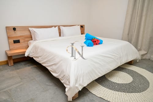 Chambre de la villa Nora chez Gerards & Angel à Grand Baie : lit en bois, draps blancs, serviettes bleues et tapis à rayures