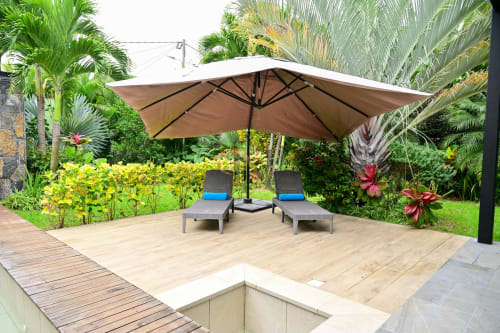 Patio de villa tropicale à Gerards & Angel avec transats sous parasol beige, jardins luxuriants et palmiers à Grand Baie