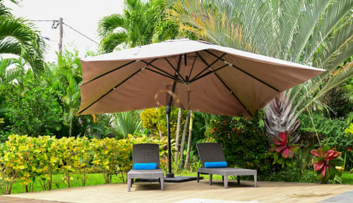 Parasol beige au-dessus de deux transats aux coussins bleus dans le jardin tropical de la villa Gerards & Angel, Grand Baie