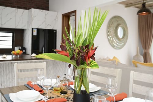 Salle à manger élégante de la villa Gerards & Angel avec composition florale tropicale, couverts dressés et cuisine moderne visible