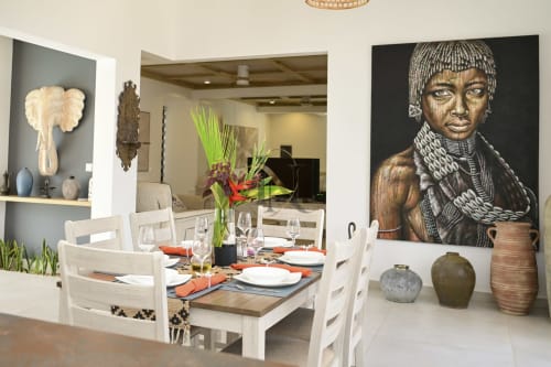 Salle à manger de villa moderne avec chaises blanches, table dressée fleurie, art africain et poteries décoratives chez Gerards &