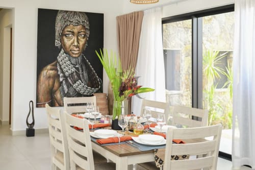 Élégante salle à manger de la villa Gerards & Angel avec table dressée, chaises blanches, art portrait africain et fleurs tropicales