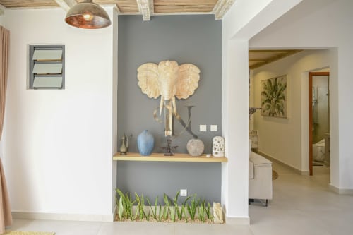 Entrée de villa moderne chez Gerards & Angel avec mur d'accent gris et étagère en bois présentant une sculpture décorative de tête d'éléphant
