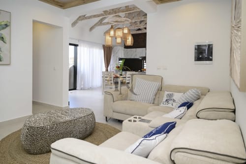 Salon moderne de villa chez Gerards & Angel avec sièges beige, poutres bois apparentes, suspensions et cuisine ouverte