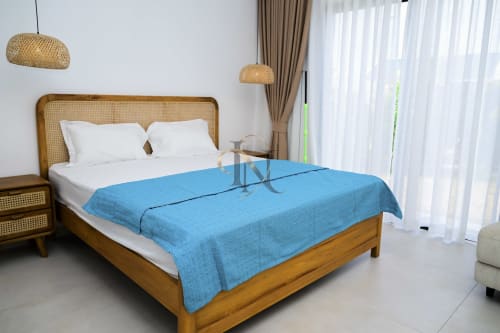 Chambre moderne avec lit en rotin, plaid bleu, luminaires en suspension tressés et rideaux voilage à la villa Gerards & Angel