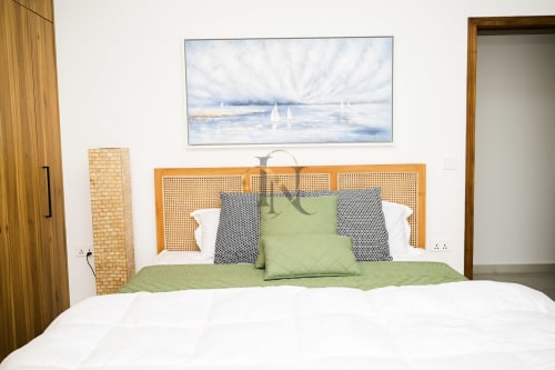 Chambre moderne de la villa Gerards & Angel avec tête de lit en rotin, literie verte, tableau voilier et accents bois à Petit