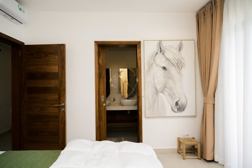 Chambre de la villa Gerards & Angel avec lit blanc, portes en bois, entrée salle de bain et tableau de cheval