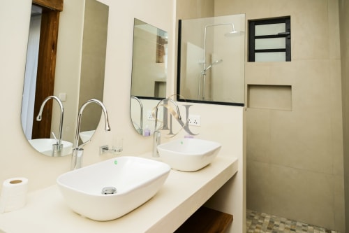 Salle de bain moderne de la villa Gerards & Angel avec vasques doubles, miroirs ronds et douche à effet pluie à Petit Raffray