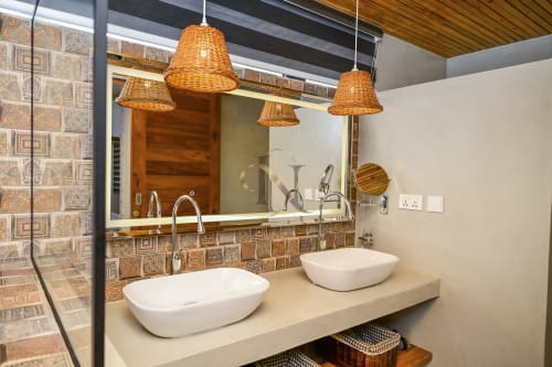 Salle de bains élégante de la villa Gerards & Angel avec vasques doubles en porcelaine blanche, luminaires suspendus tressés et dosseret en carrelage décoratif