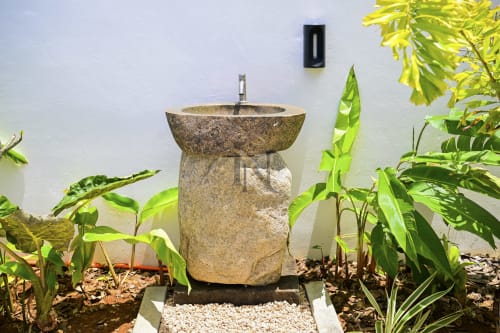 Lavabo en pierre sur socle entouré de plantes luxuriantes à la villa Gerards & Angel à Maurice