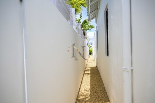 Étroit passage aux murs blancs de la villa Gerards & Angel à l'Île Maurice avec palmiers visibles au loin