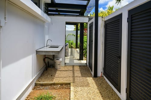 Couloir de villa moderne avec vasque, sol en gravier et portes de rangement à persiennes noires ouvrant sur la cour-jardin de Gerards &