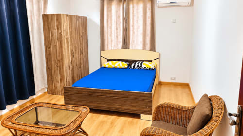 Bedroom at Martello Residence Apt 1 in La Preneuse with wooden bed, blue bedding, wicker seating area, and wooden wardrobe.