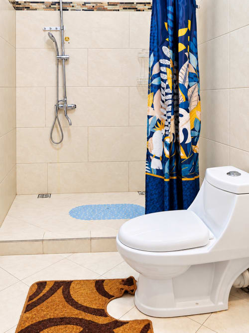Modern bathroom at Gerards & Angel in La Preneuse with white toilet, walk-in shower, colorful curtain, and beige tilework.