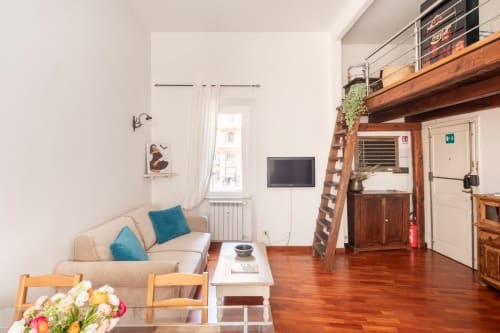 Appartement cosy à Rome avec canapé beige, coussins bleus, mezzanine en bois, TV et parquet
