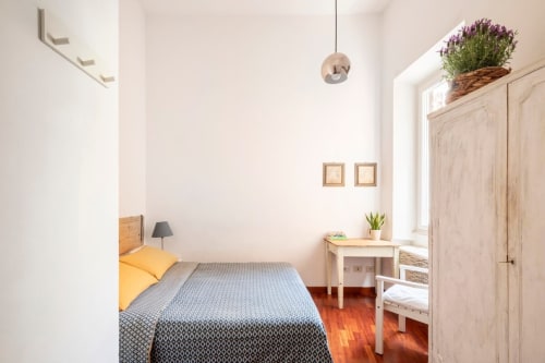 Chambre lumineuse dans une location à Rome avec literie jaune, mobilier en bois, plantes en pot et parquet