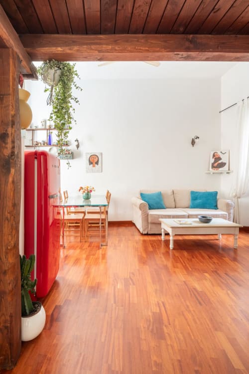 Lumineux appartement romain aux poutres en bois, réfrigérateur rouge, canapé crème avec coussins bleus et coin repas